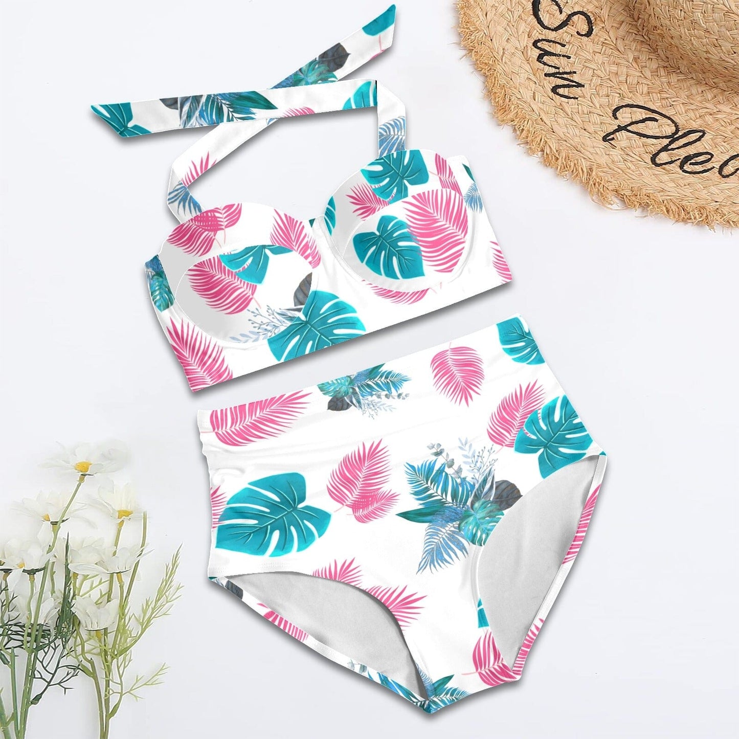 Tropical leaf patterned swimsuit on a white background with a straw hat and flowers.