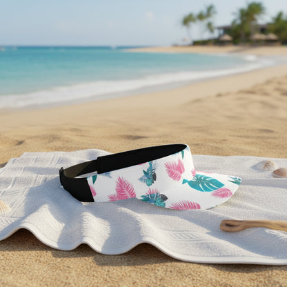 White sun visor with black elastic strap with colorful leaf pattern on a white towel with a beach background