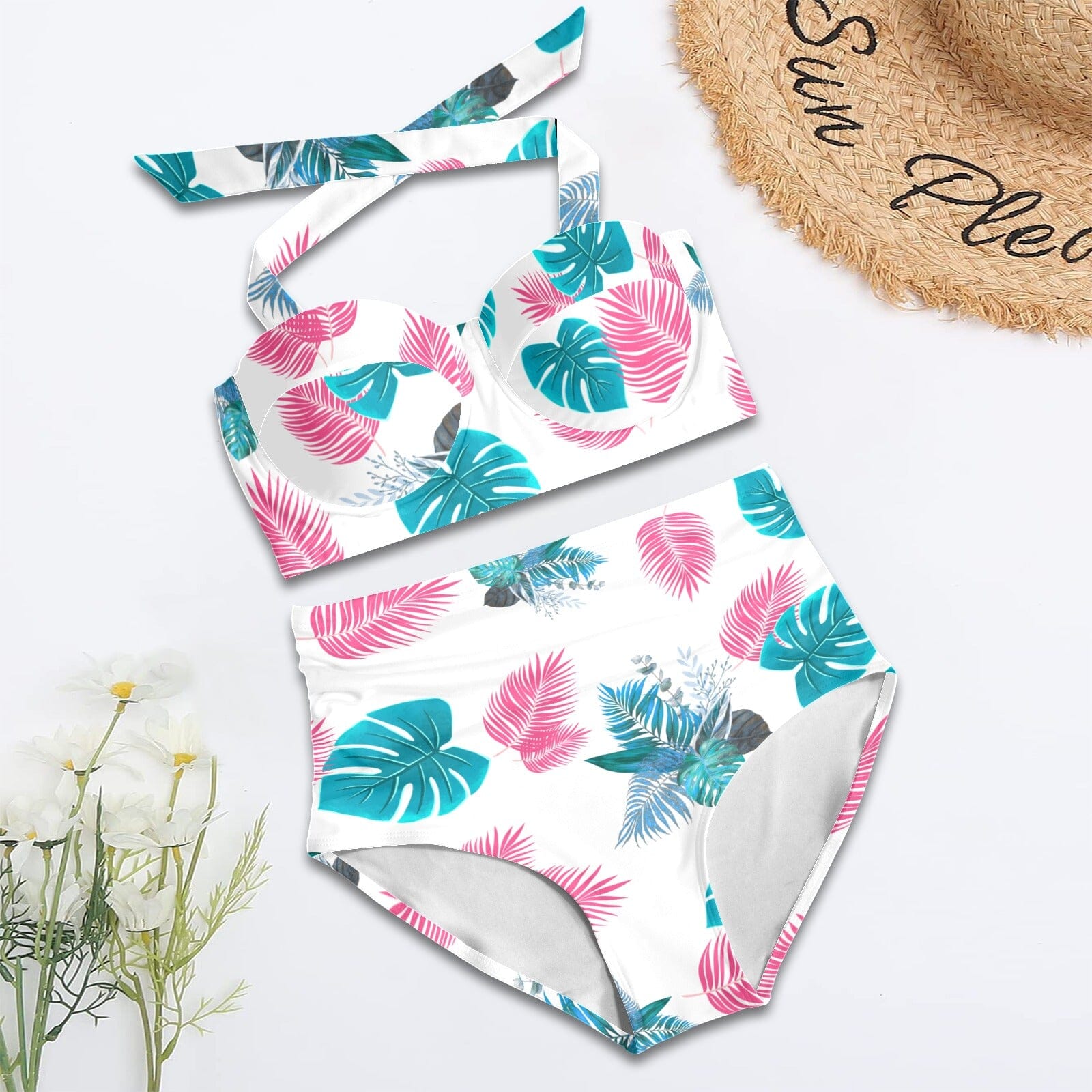 Tropical leaf patterned swimsuit on a white background with a straw hat and flowers.